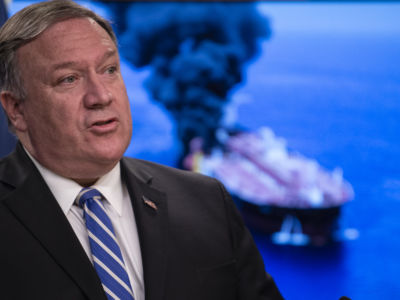 Mike Pompeo stands in front of a photo of a burning tanker, oil