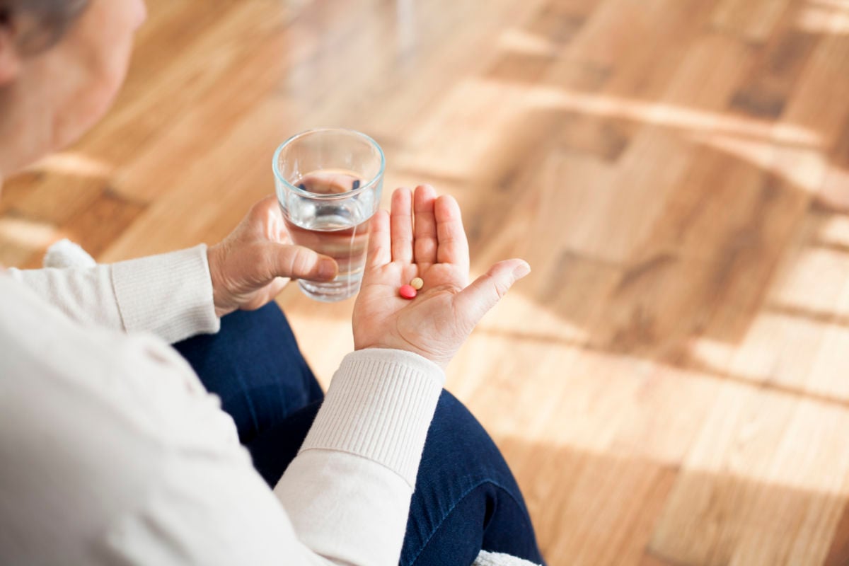 A person holds pills in one hand and a glass of water in the other