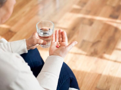 A person holds pills in one hand and a glass of water in the other