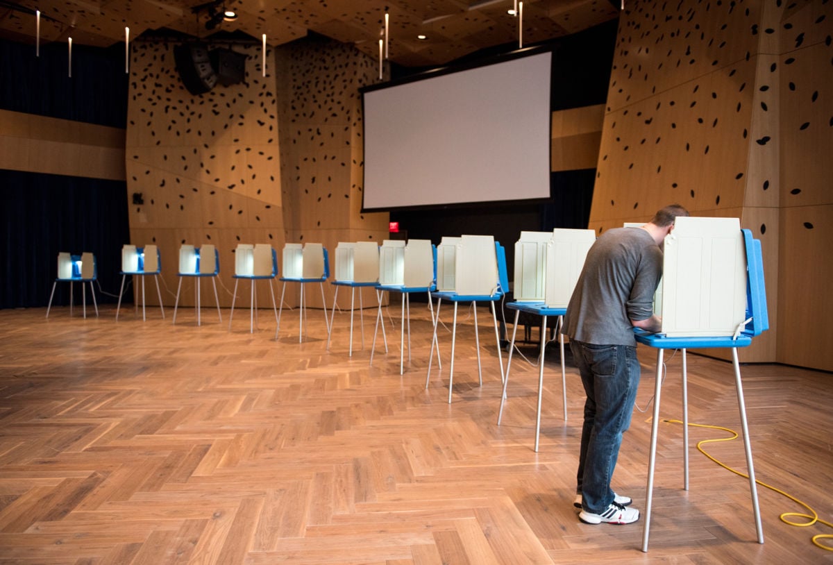 A man votes at one of many voting booths, the rest around him empy