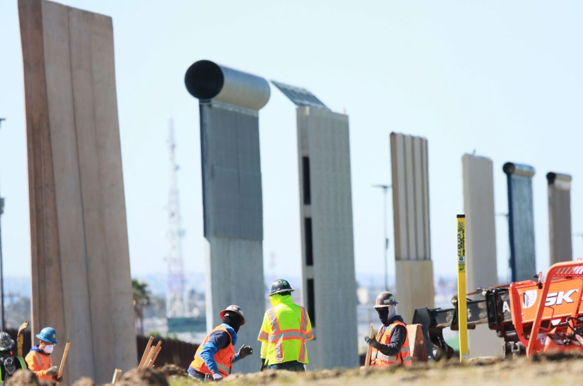 Construction workers build a secondary border wall with prototype models standing behind on February 22, 2019, in Otay Mesa, California.