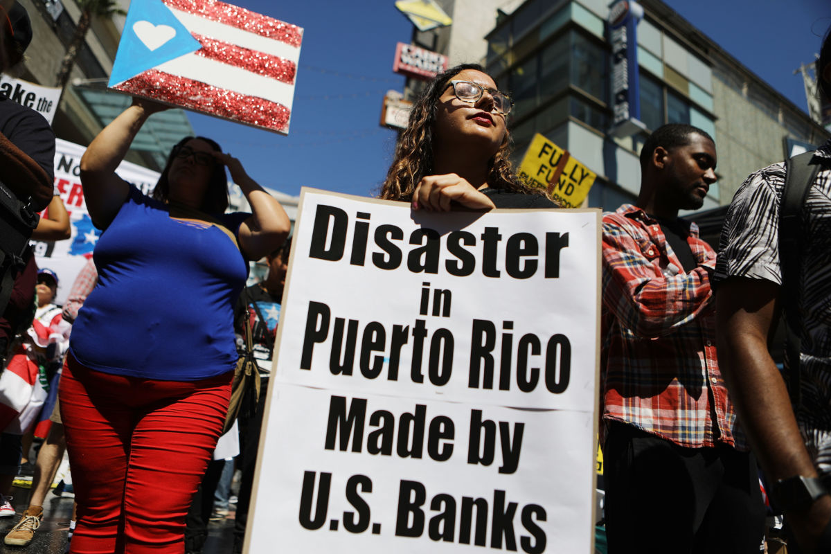 A woman holds a sign reading "Disaster in Puerto Rico made by U.S. banks"