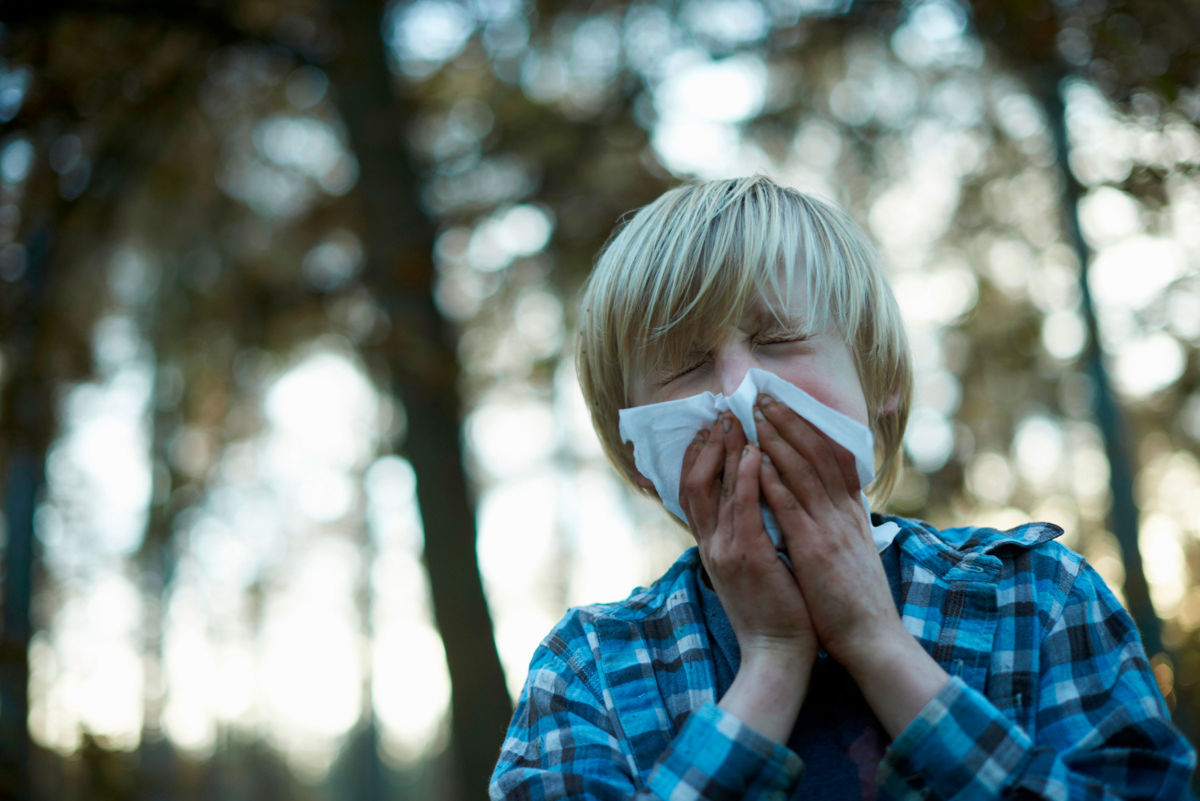Boy sneezing into tissue outdoors.