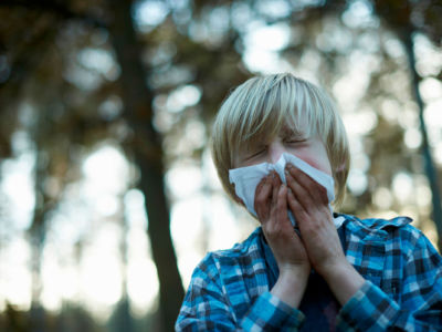 Boy sneezing into tissue outdoors.
