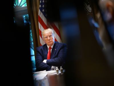 Donald Trump sits at a table with his arms crossed