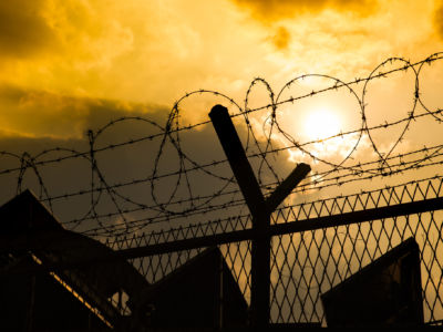 A barbed wire fence is seen backlit from a yellow sunset, prison