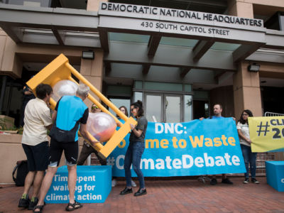 A group of people flip over an hourglass in front of the Democratic National Committee headquarters, during a Green Peace rally to call for a presidential climate debate on June 12, 2019, in Washington, D.C.