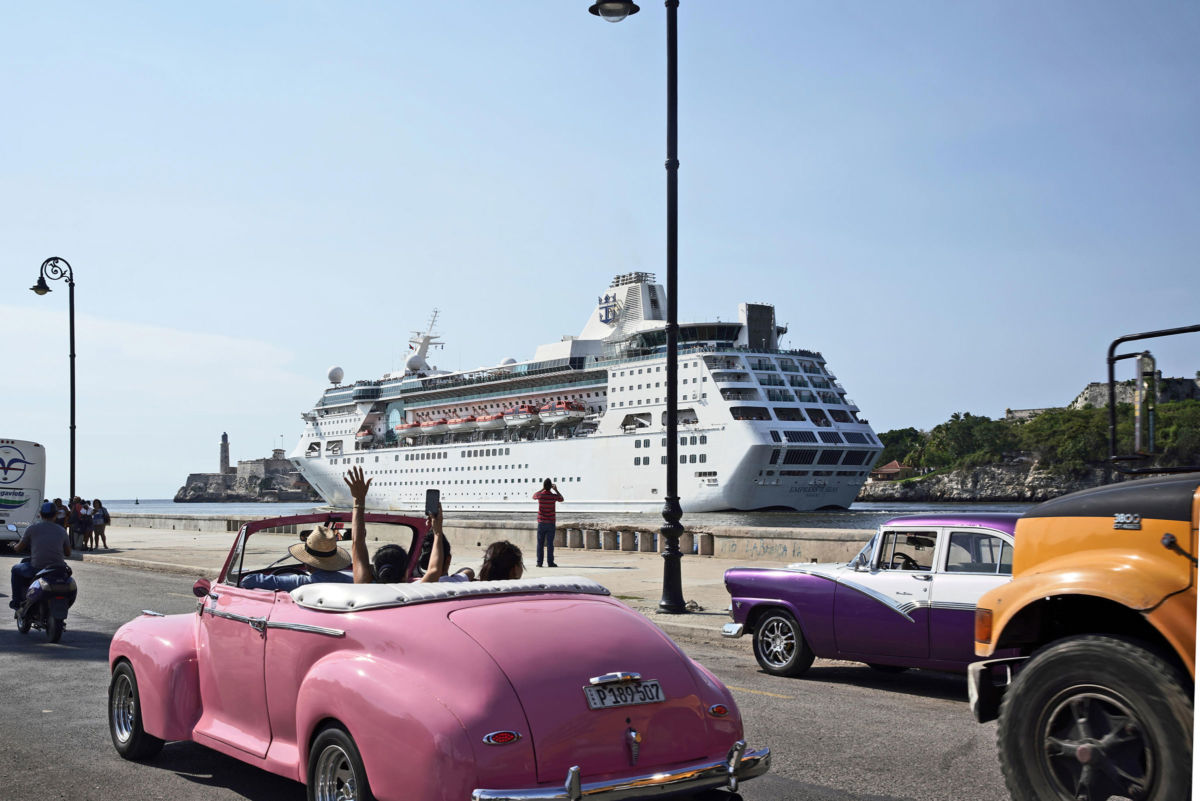 Tourists riding in a vintage car wave to the Empress of the Sea of Royal Caribbean International as it leaves the harbor of Havana on June 5, 2019, in Havana, Cuba.