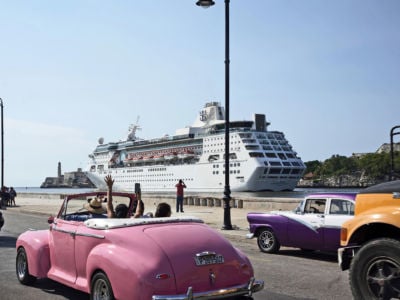 Tourists riding in a vintage car wave to the Empress of the Sea of Royal Caribbean International as it leaves the harbor of Havana on June 5, 2019, in Havana, Cuba.