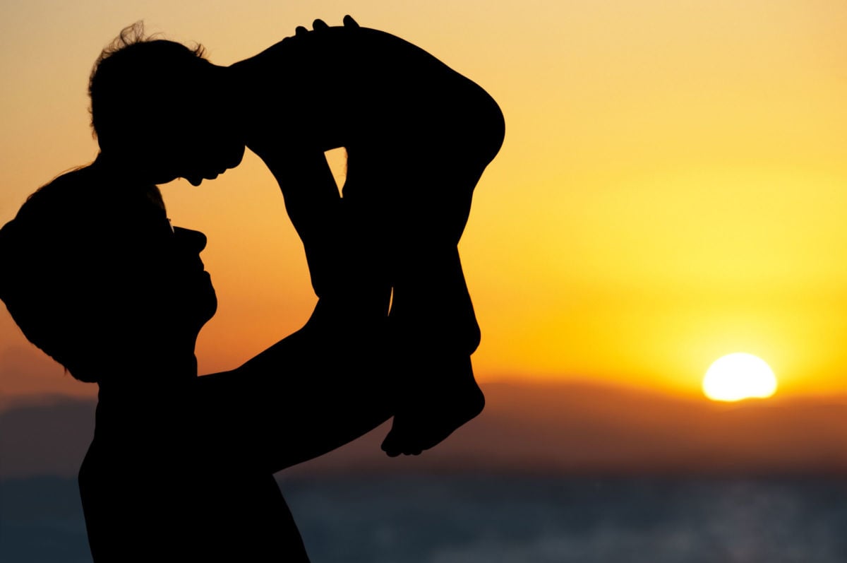 Father lifts child, silhouetted against sunset