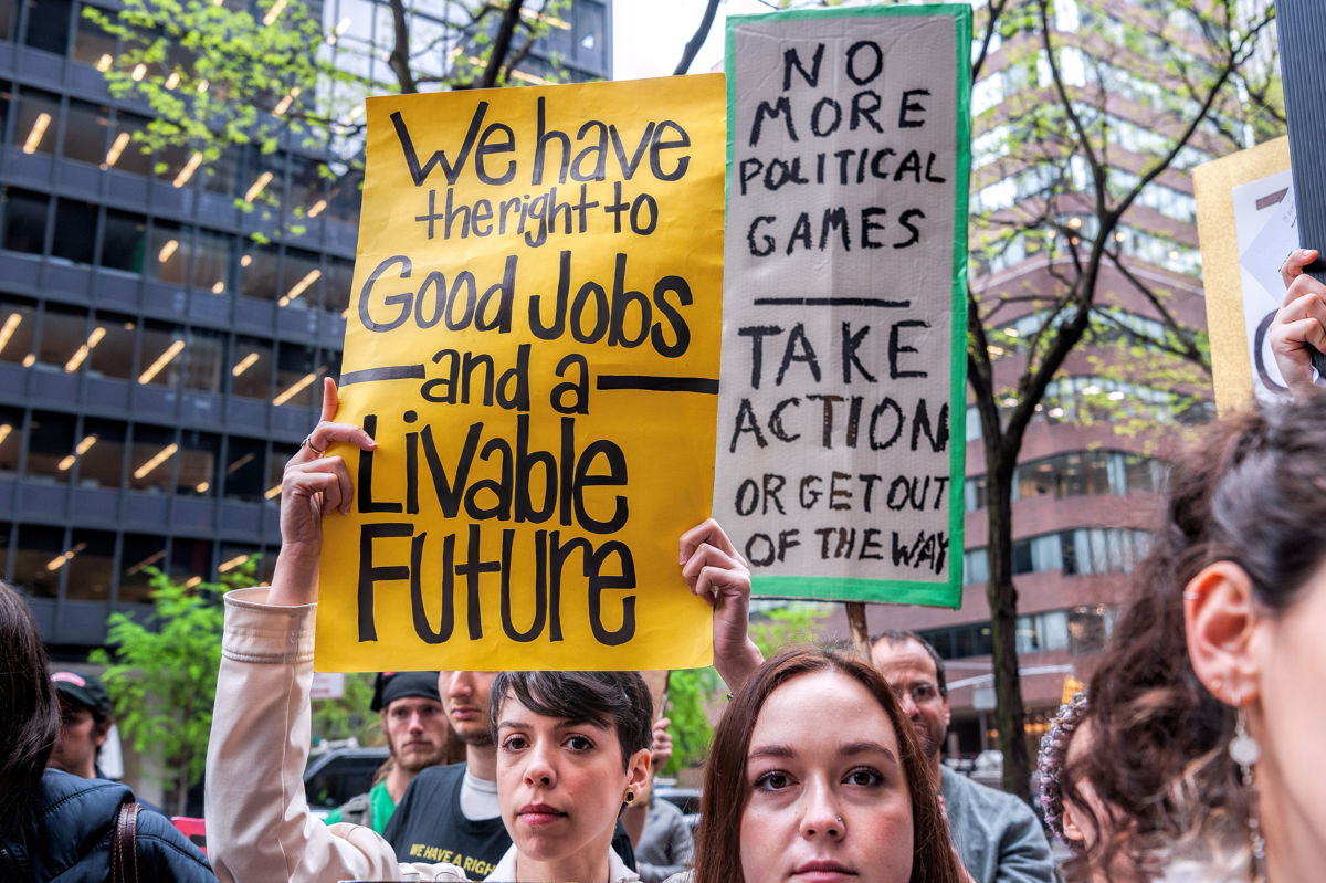 A woman holds a sign reading "We have the right to good jobs and a livable future" while at a rally