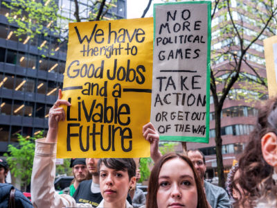 A woman holds a sign reading "We have the right to good jobs and a livable future" while at a rally