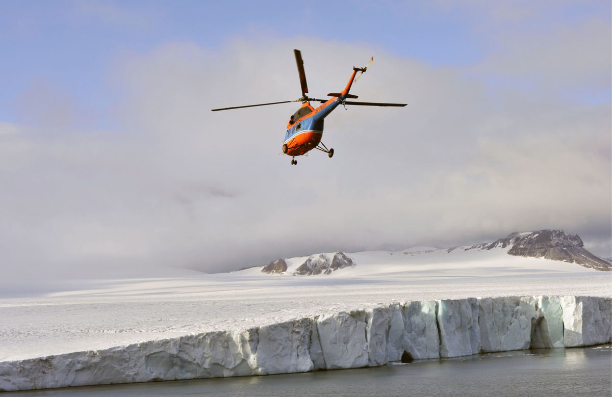 A helicopter flies over a glacier on the Franz Josef Land Archipelago in the Arctic Ocean, August 23, 2017.