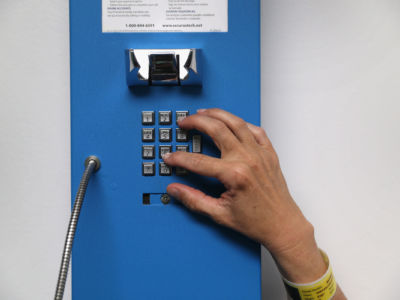 A hand reaches up to dial the numbers on a blue prison phone