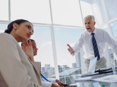 An angry boss towers over his employees while shouting