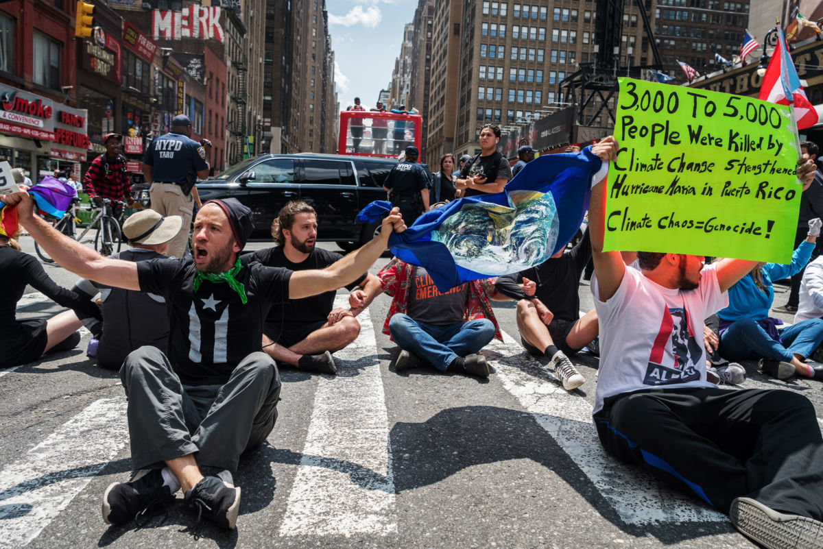 Protesters sit in a busy street and chant while holding signs, climate