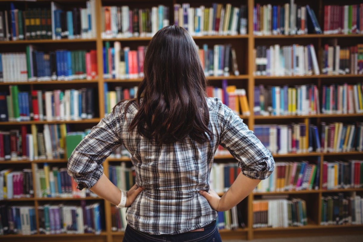 A young woman looks at shelves of books in a library