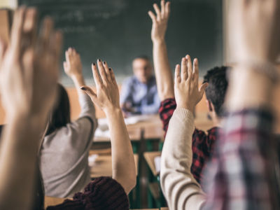 Students raise hands in college classroom