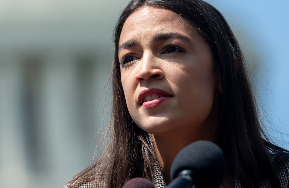 A close up of Alexandria Ocasio-Cortez's face with the capitol dome in the background