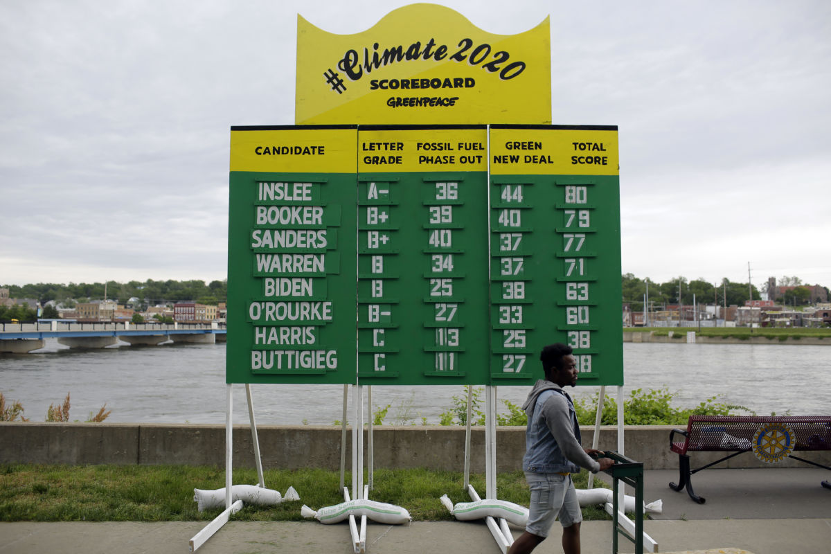 A person walks by a scoreboard listing various Democratic presidential candidates' "grades" with regard to their policy stance on climate change