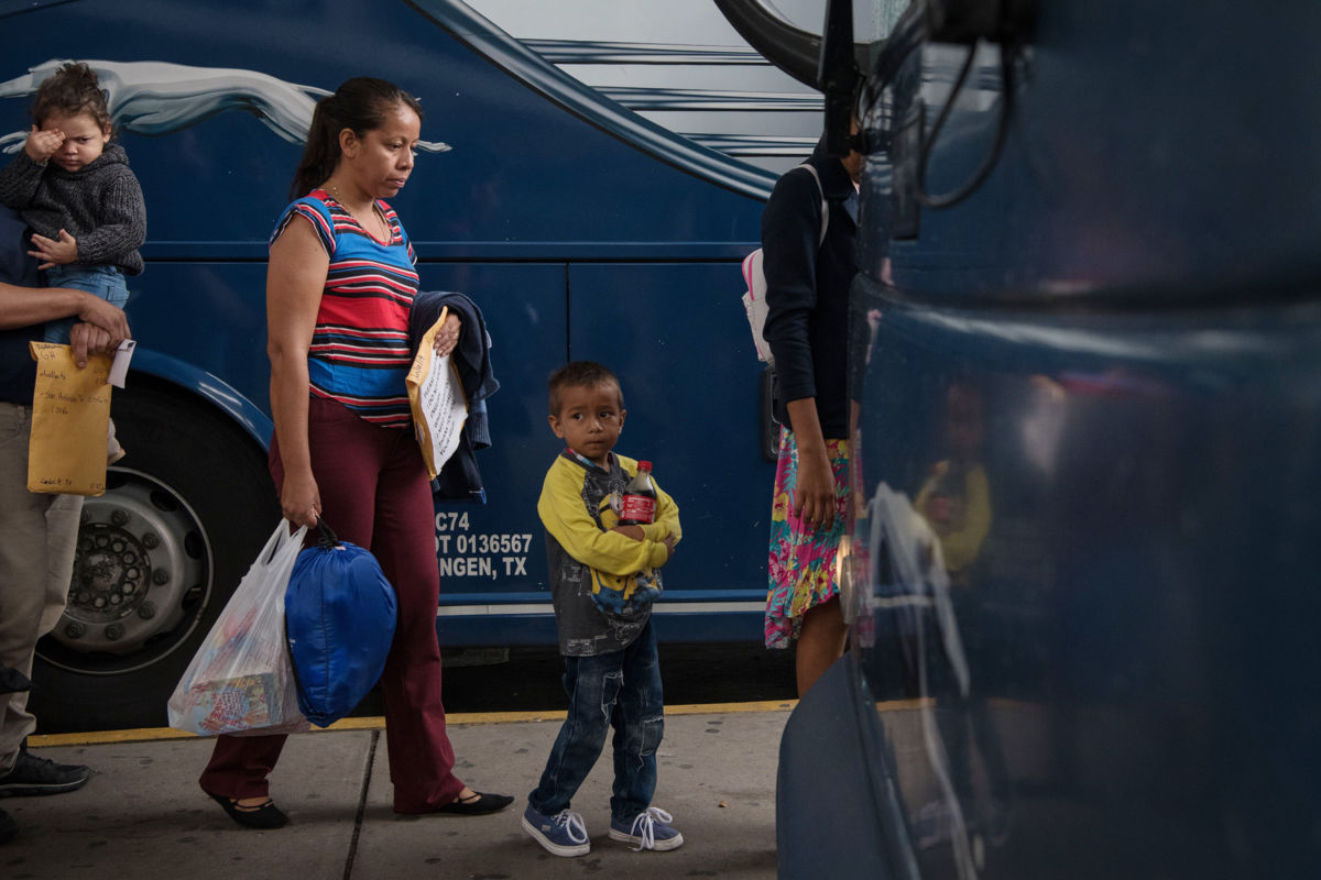 A young boy walks with his mother toward a greyhound bus, migrant detention