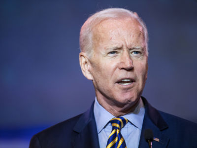 Joe Biden squints into an apparent source of light while speaking into a microphone