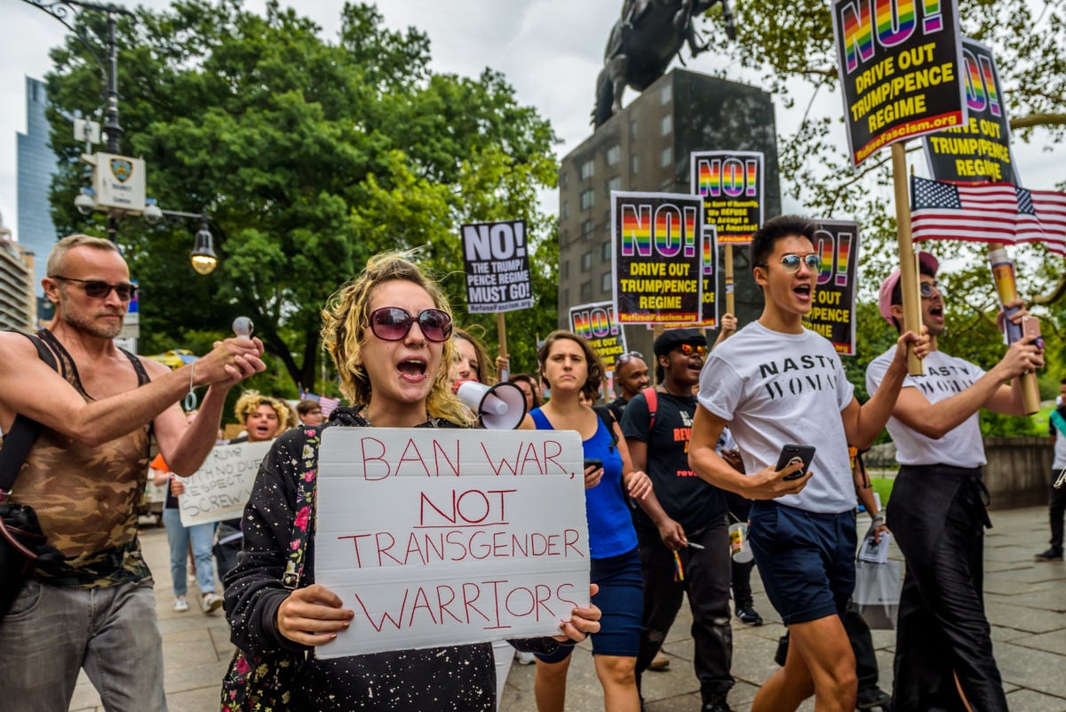 A protester holds a sign reading "BAN WAR NOT TRANSGENDER WARRIORS" during a protest