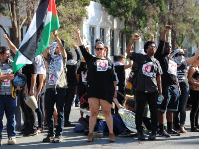 People wearing black and holding Palestinian flags stand in a small crowd