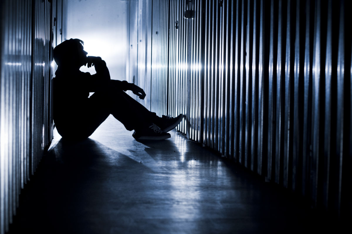 A youth sits amidst cells while silhouetted by blue light