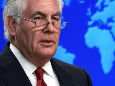 Rex Tillerson stands in front of a blue display with Earth's continents on it