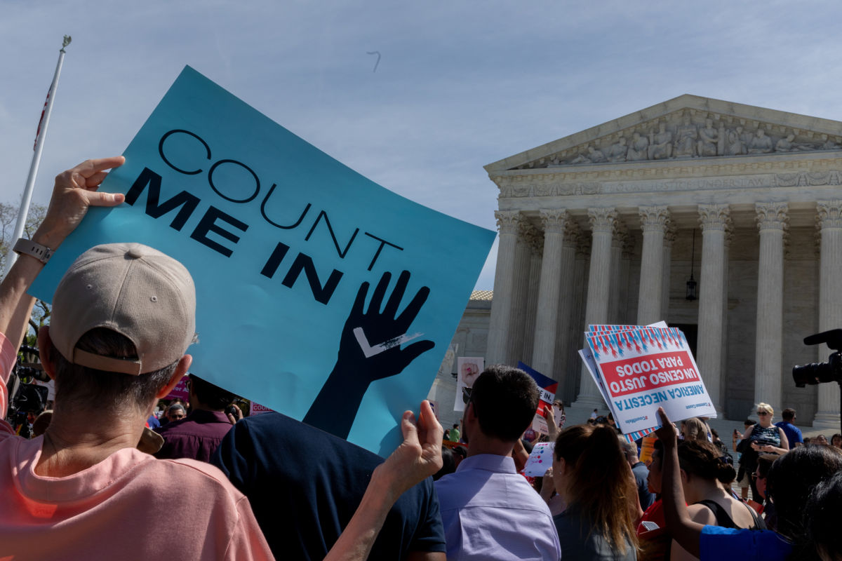 A person holds a blue sign reading "COUNT ME IN" in front of the U.S. Supreme Court building