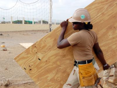 A Black construction worker carrying plywood.