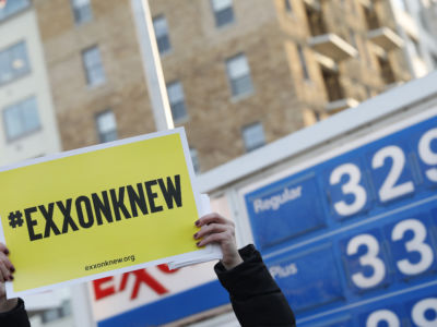 A protester holds a yellow sign reading "EXXON KNEW" during a demonstration