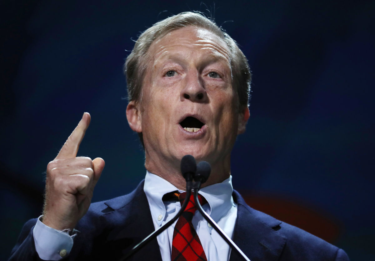 Tom Steyer points a finger upward while speaking at an event