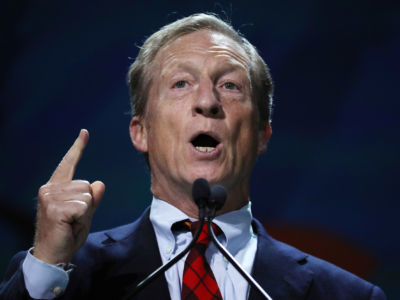 Tom Steyer points a finger upward while speaking at an event
