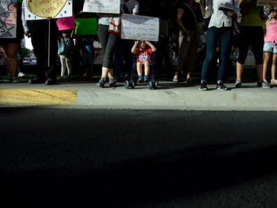 A child in a stroller holds a sign as people rally outside the El Paso County Detention Center, June 21, 2018, in El Paso, Texas.