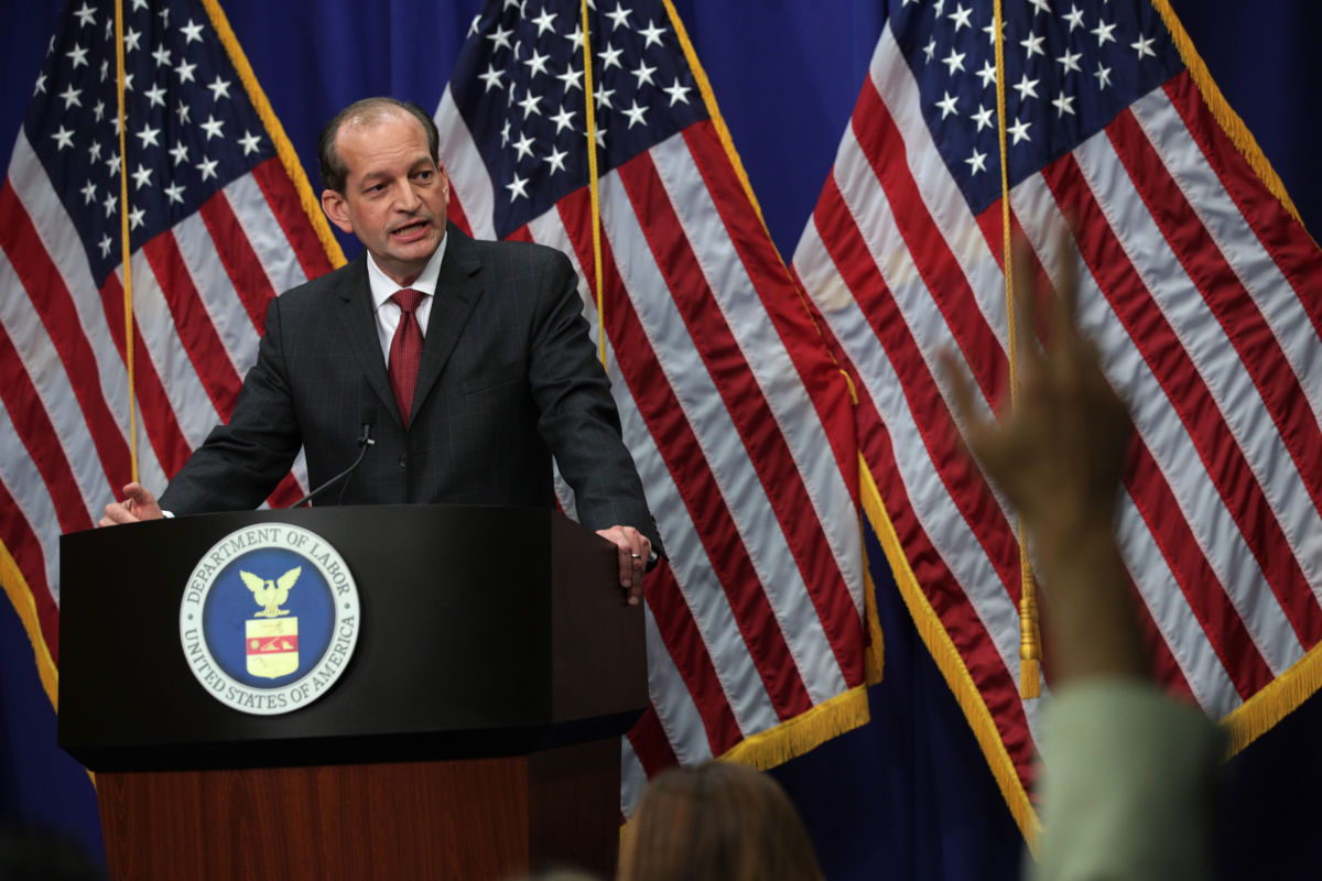 Alex Acosta stands at a podium as reporters raise their hands with questions