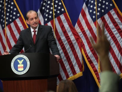 Alex Acosta stands at a podium as reporters raise their hands with questions