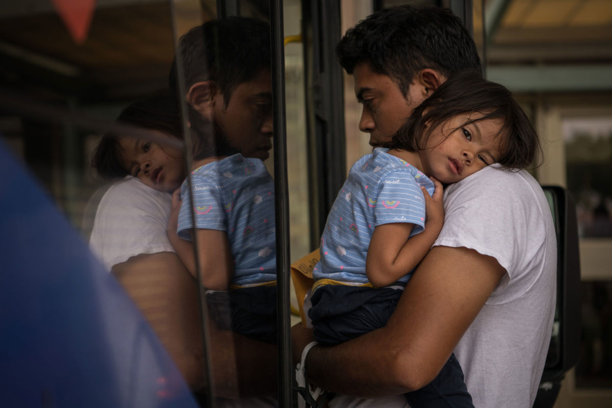 A Honduran migrant recently released from a federal immigrant jail boards a bus while carrying his 2-year-old daughter at a bus depot on June 11, 2019, in McAllen, Texas.