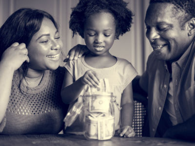 Parents watch their daughter put money in jar for savings