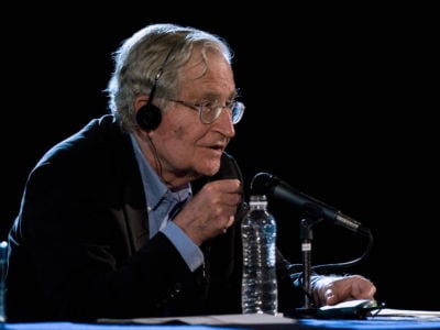 Noam Chomsky speaks into a microphone while seated