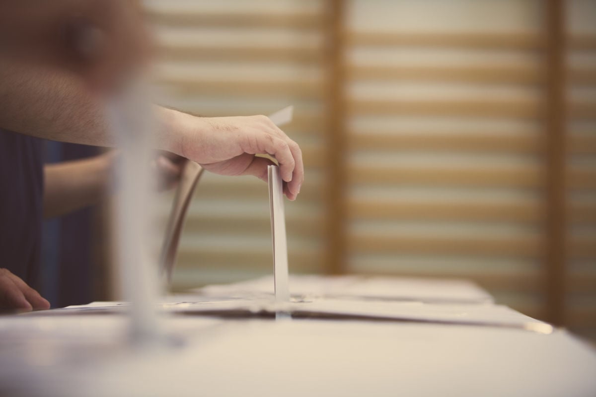 A hand puts paper into a ballot box