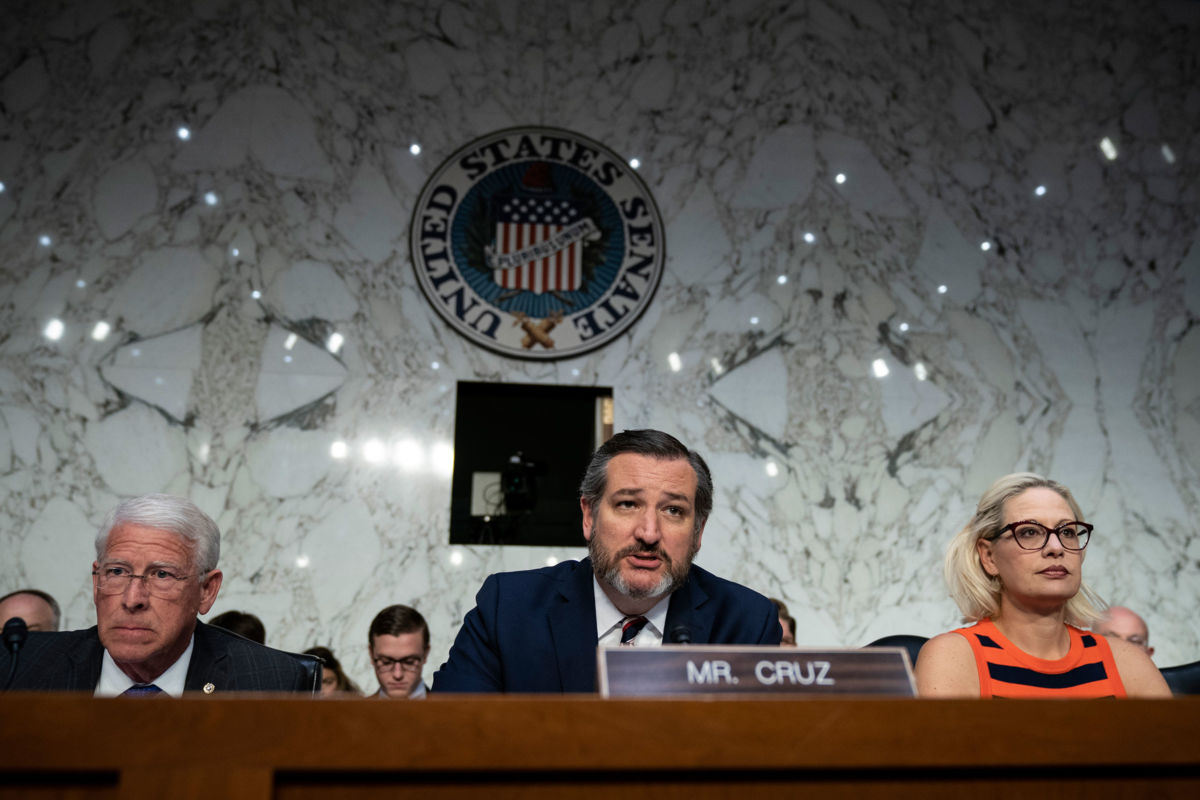 Ted Cruz sits between two other senators and speaks into a microphone