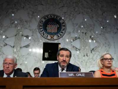 Ted Cruz sits between two other senators and speaks into a microphone