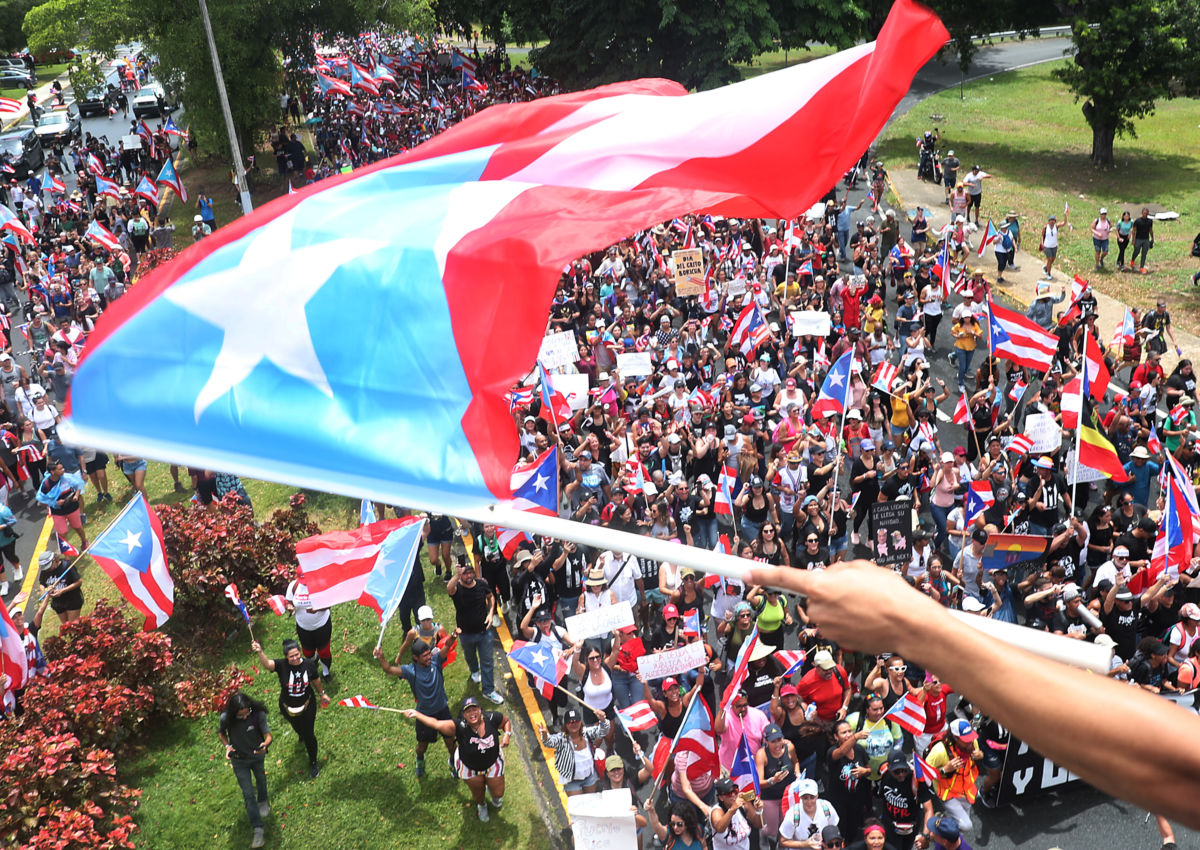 Protesters fill the streets as a person waves a Puerto Rican flag in the foreground