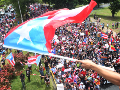 Protesters fill the streets as a person waves a Puerto Rican flag in the foreground