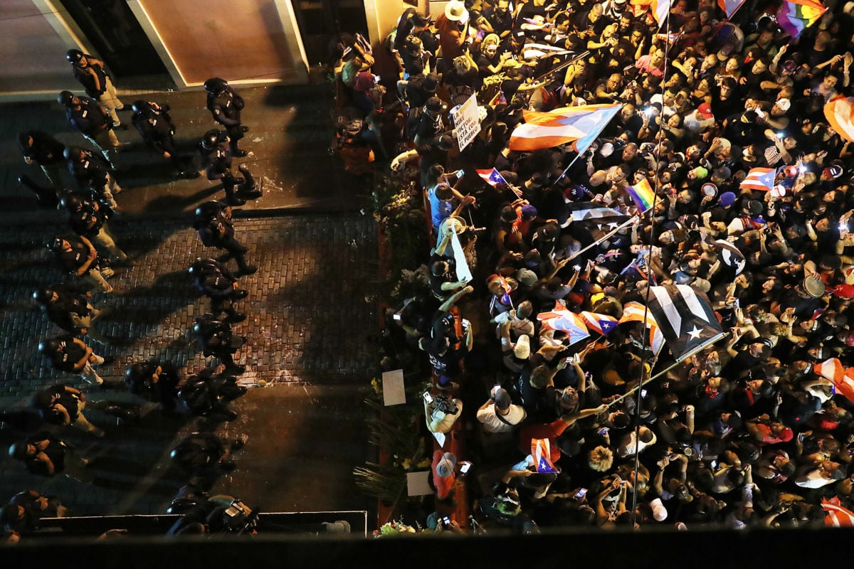 A line of armored police blocks the progress of a crowd of protesters