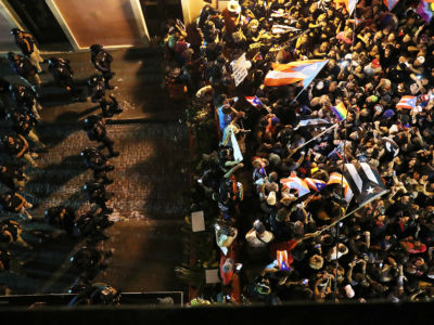 A line of armored police blocks the progress of a crowd of protesters