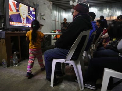 Migrants view a live televised speech by President Trump at a shelter for migrants on January 8, 2019, in Tijuana, Mexico.