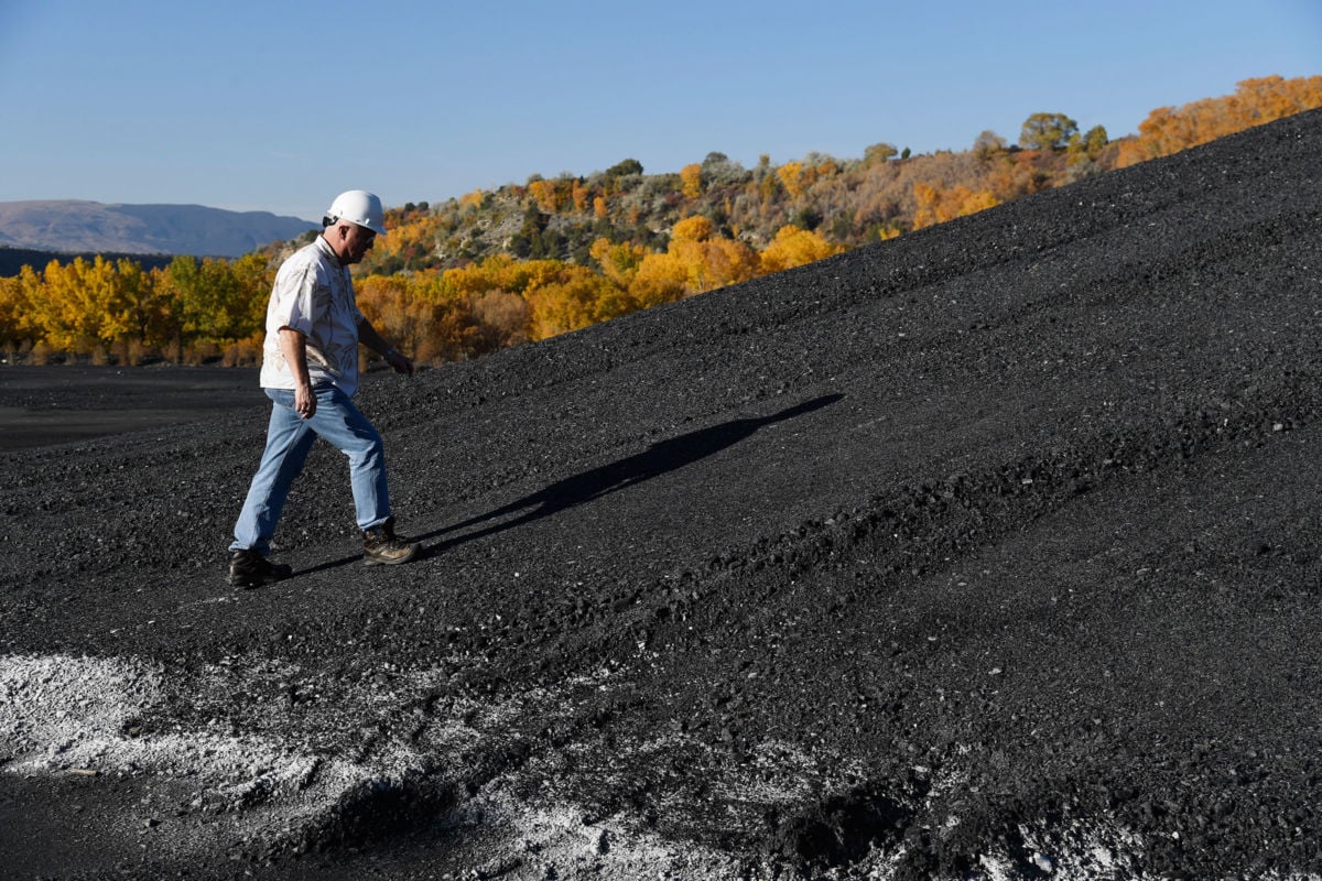 A man in a hard hat walks up a hill of coal